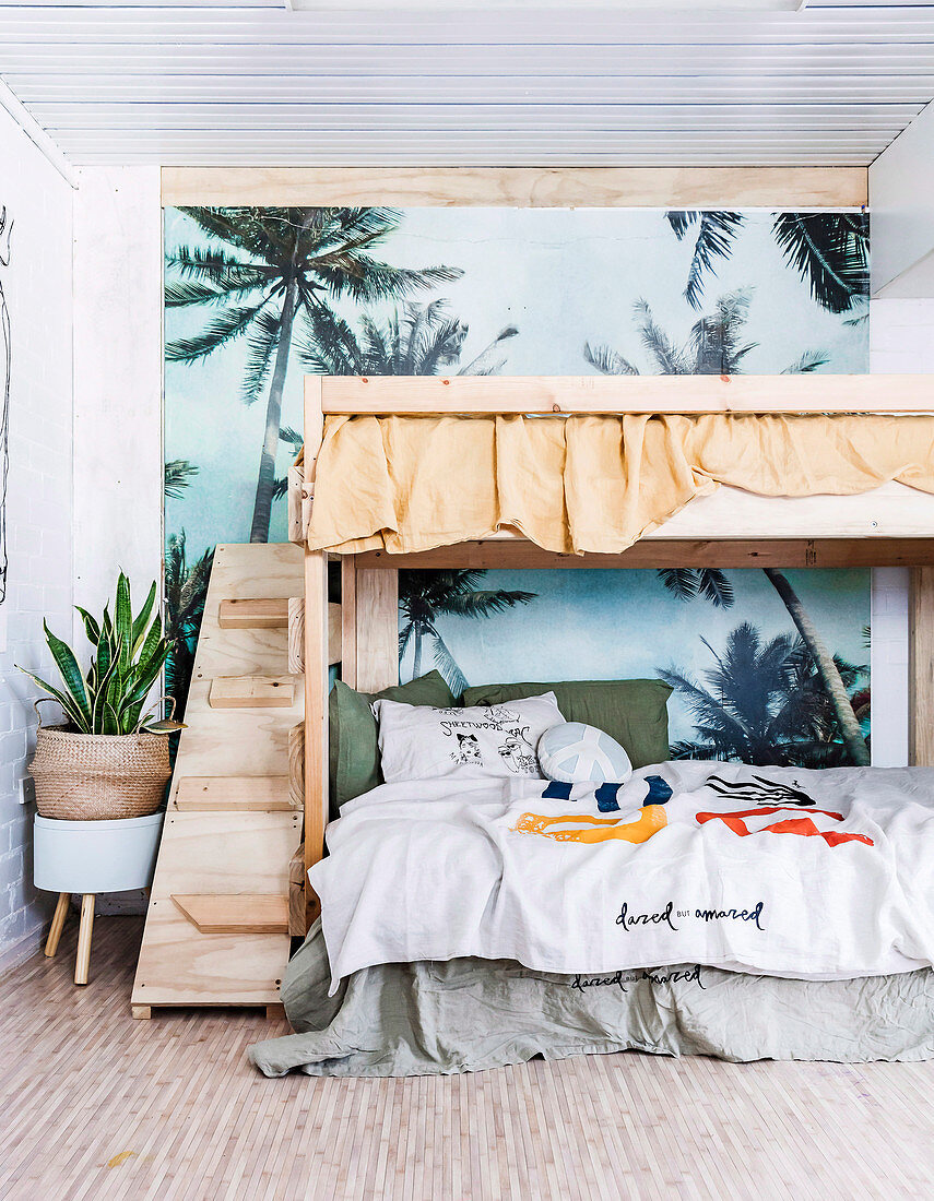 Wooden bunk bed in front of palm tree wallpaper in the children's room