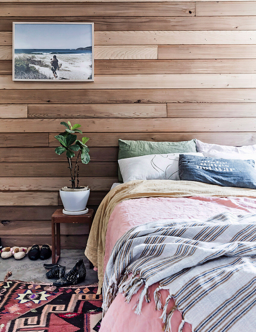 Doppelbett und Nachttisch mit Zimmerpflanze vor Wandverkleidung aus recyceltem Zedernholz