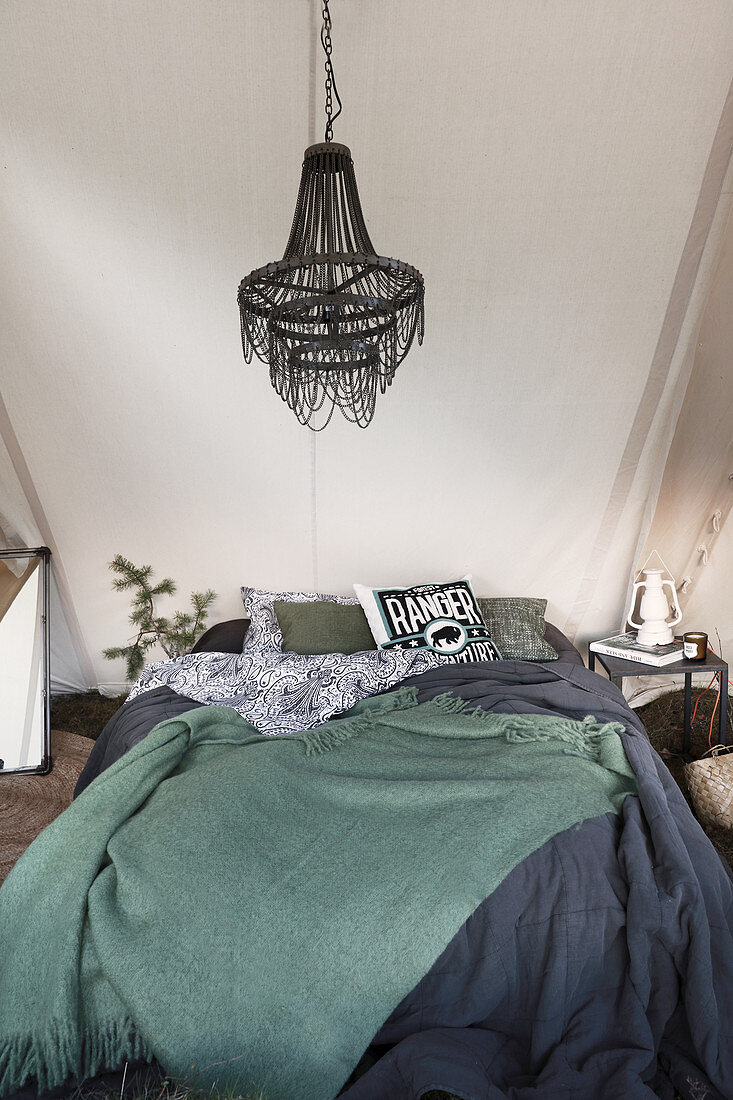 Bett mit dunklen Decken, darüber Kronleuchter im Zelt