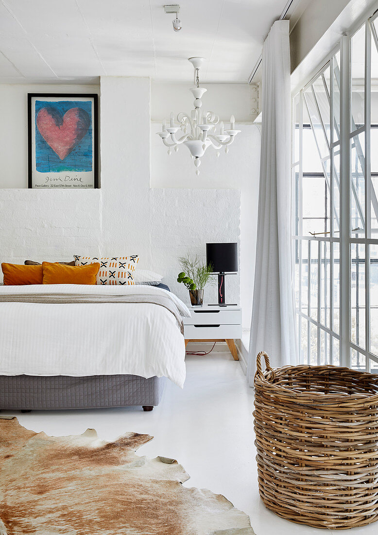 Double bed, cowhide rug and basket in white bedroom