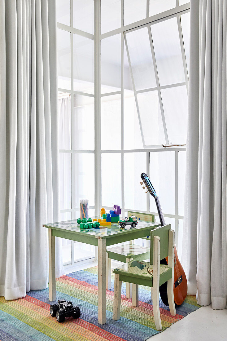 Toys on child's table, chairs and guitar next to window in high-ceilinged room