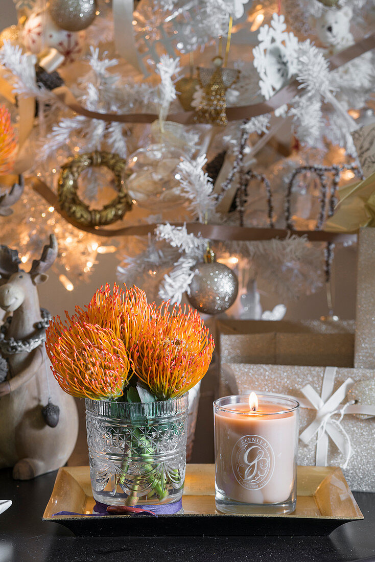 Vase of orange proteas and candle in jar on golden tray