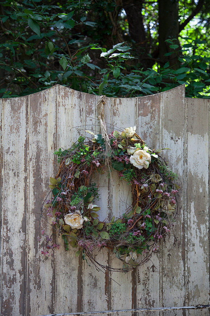 Kranz mit Blüten an rustikalem Holzzaun im Garten