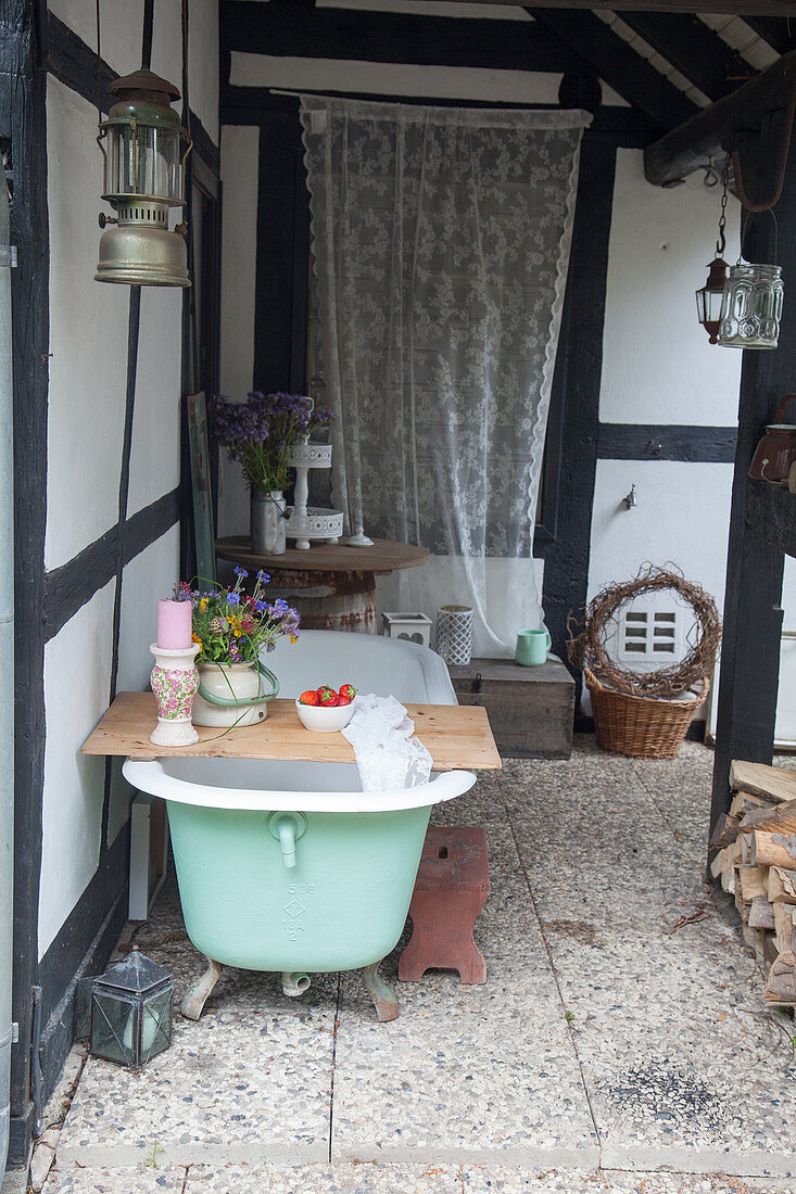 Nostalgische Badewanne mit Kerze und Blumenstrauß auf überdachter Veranda