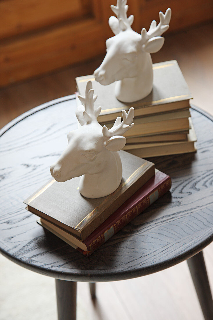 Stoneware stags heads on two stacks of books on small round table