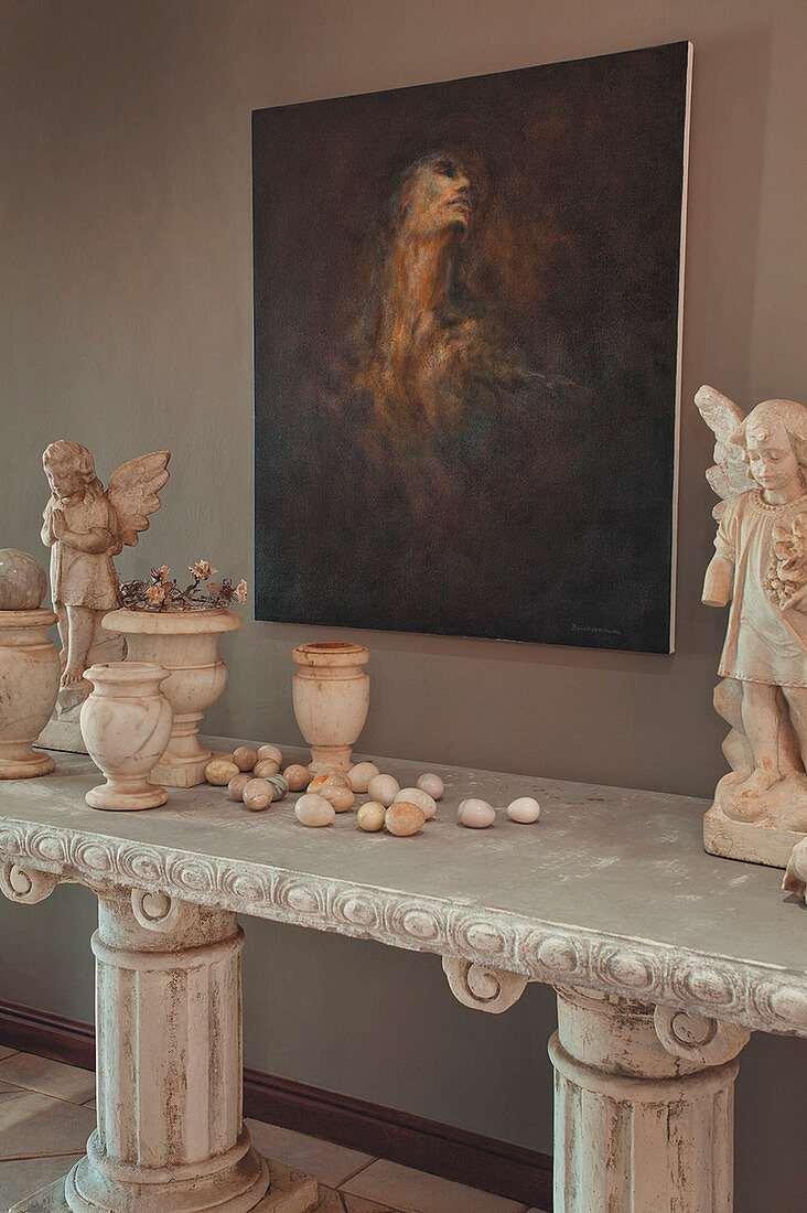 Painting on wall above angel figurines, urns and eggs on stone table