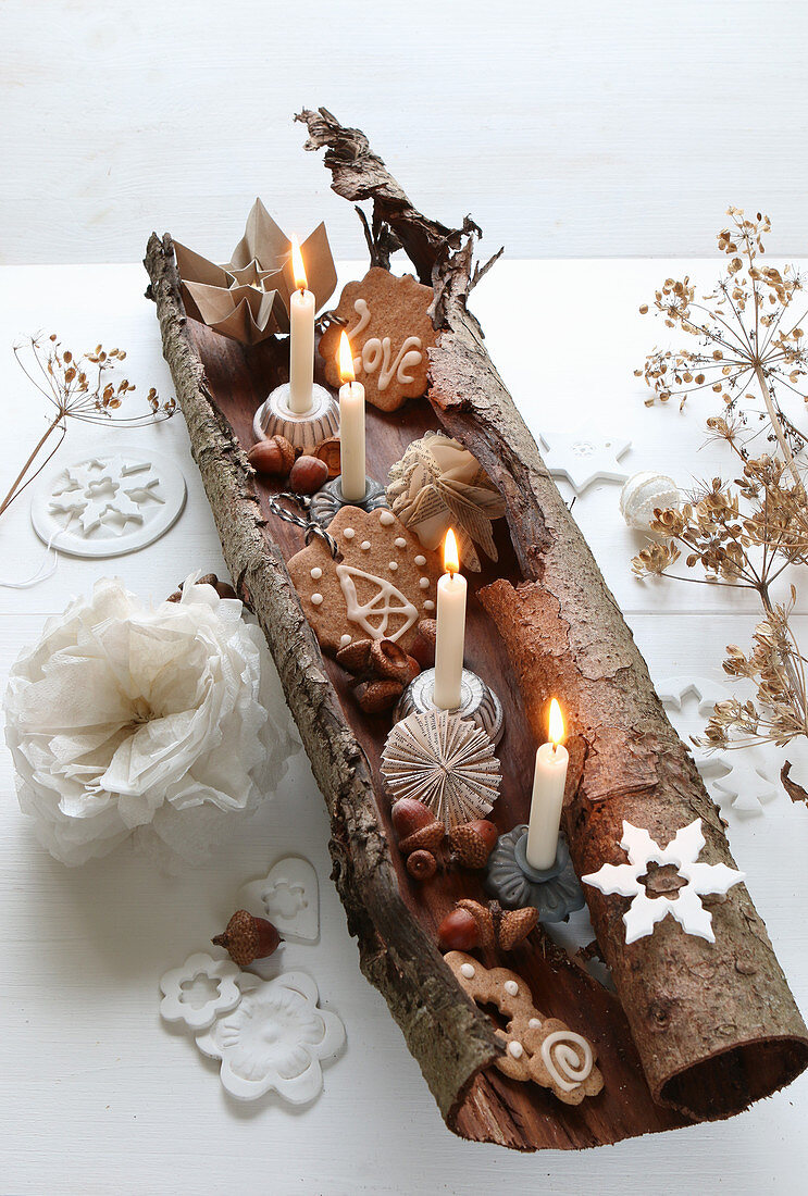 Vier brennende Kerzen, Eicheln und Kekse in gerollter Baumrinde