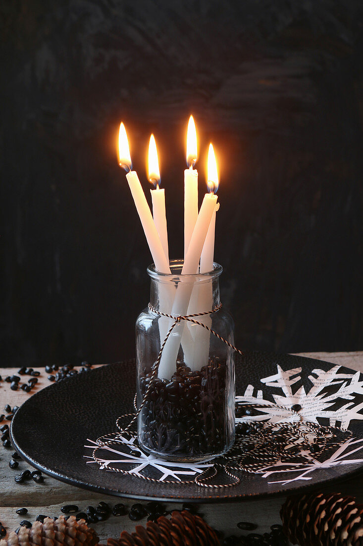 Brennende Kerzen in einem Glas mit schwarzen Bohnen vor schwarzem Grund