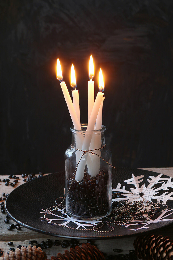 Lit candles in jar of black beans against black background