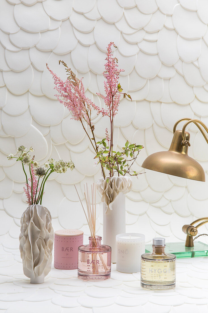 Still-life arrangement of sculptural vases and home fragrances against structured wallpaper