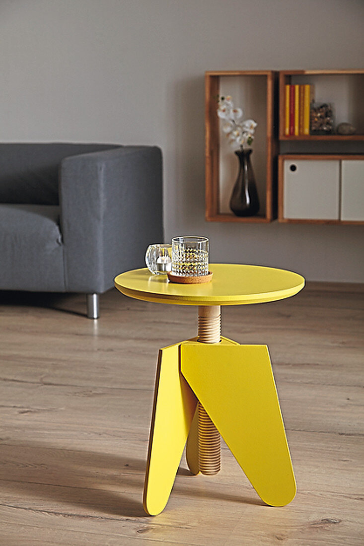 Bright yellow, three-legged stool with threaded rod used as side table