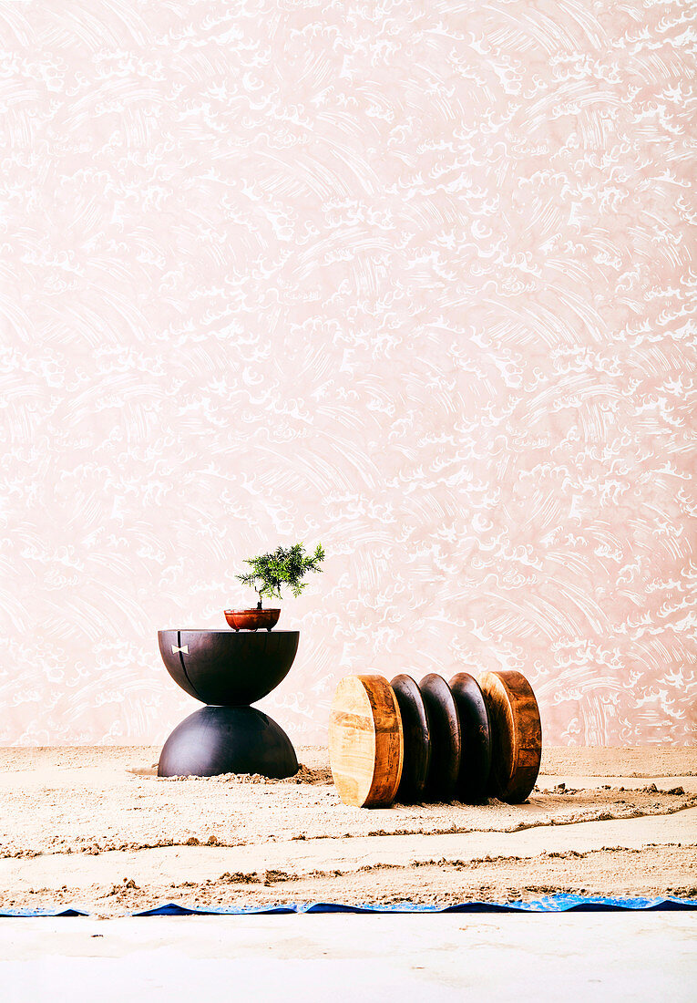 Designerhocker aus Holz auf Sandboden vor rosafarbener Tapete