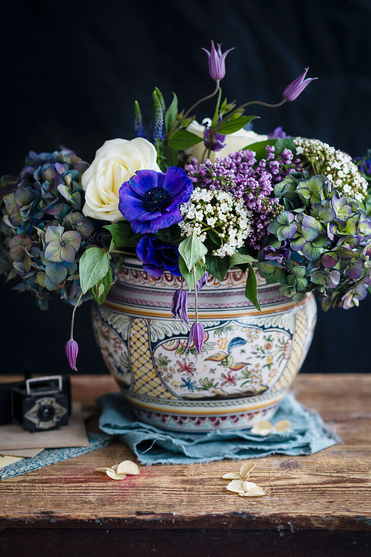 Arrangement of blue, purple and white flowers in china vase against black background