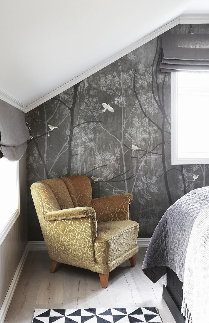 Old armchair against grey wallpaper below sloping ceiling