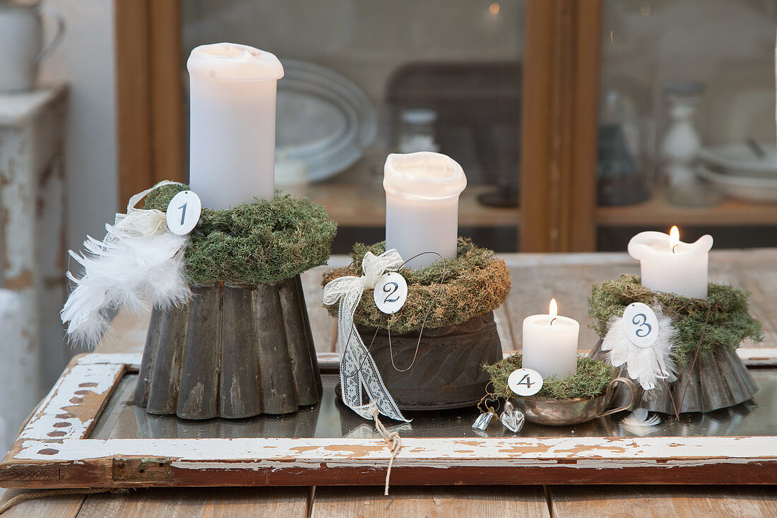 Adventskranz aus vier Kerzen auf alten Backformen mit Moos