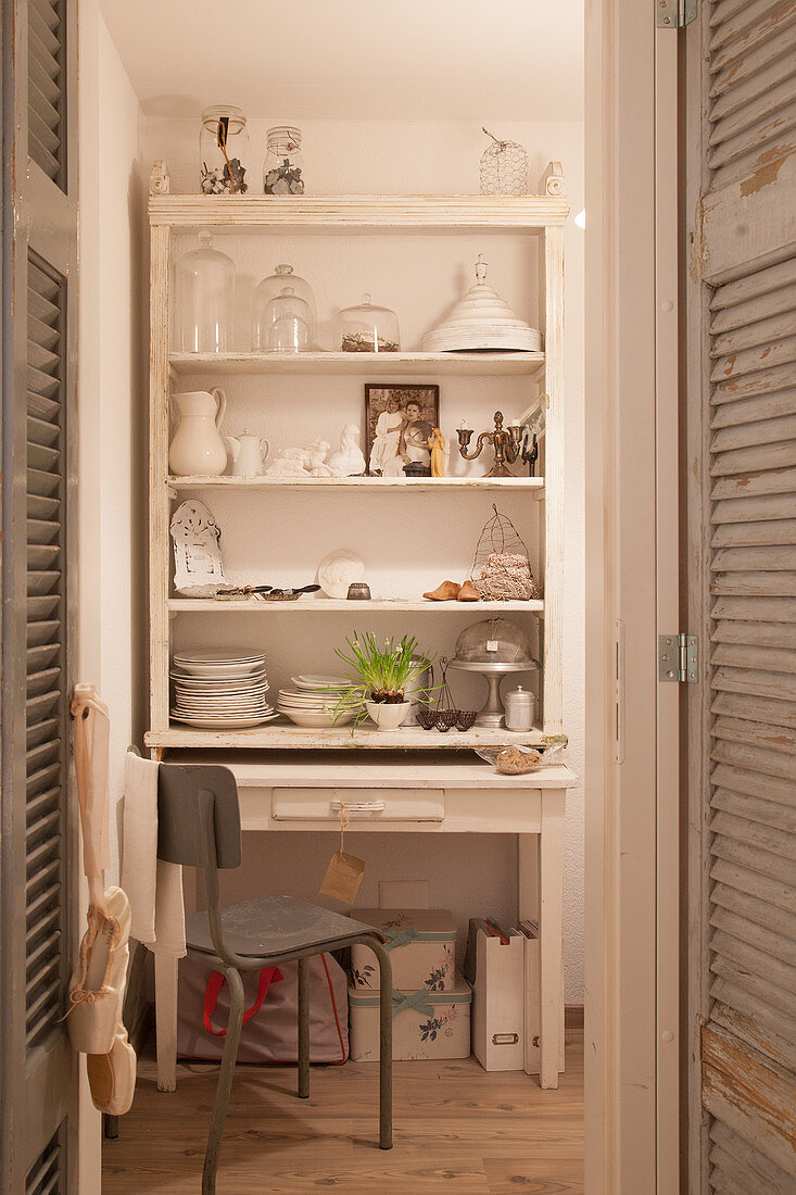 View of table and shelves of crockery behind window shutters