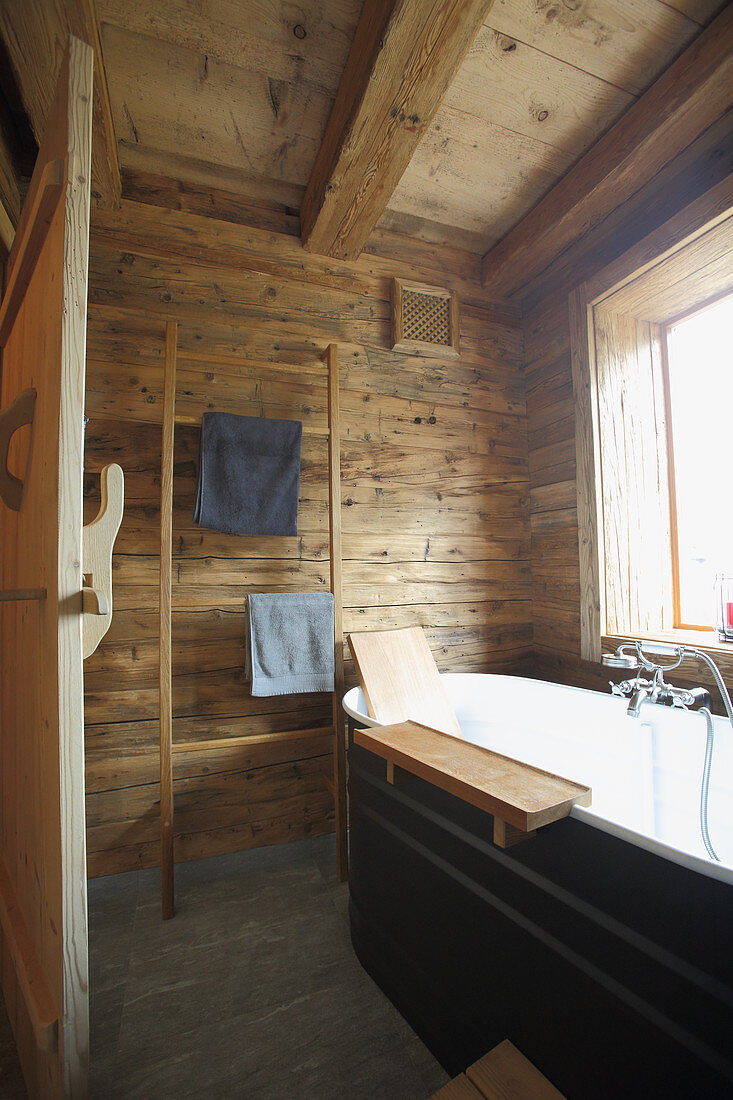 Bathtub and towel rail in rustic, wood-clad bathroom
