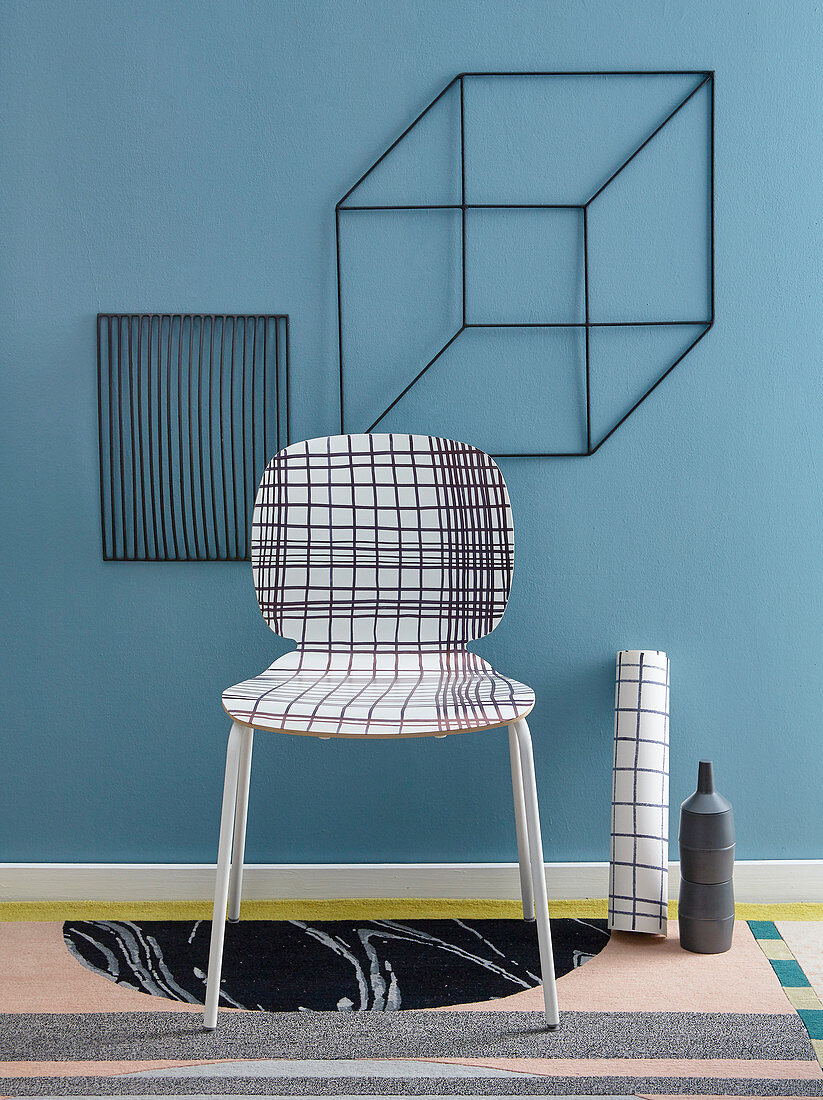 Stuhl mit kariertem Klebefolie überzogen und Würfelform aus Metall an der Wand