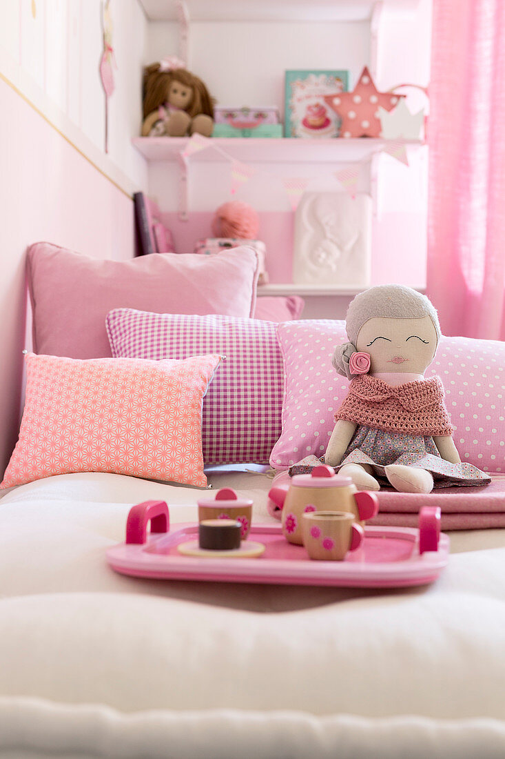 Dolls' tea set on tray and doll on bed with pink scatter cushions