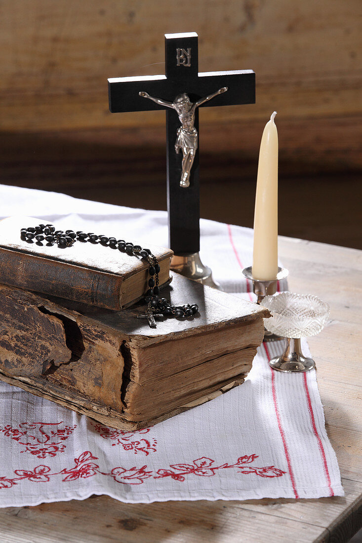 Alte Bücher, Kruzifix, Rosenkranz, Glas und Kerze auf Holztisch