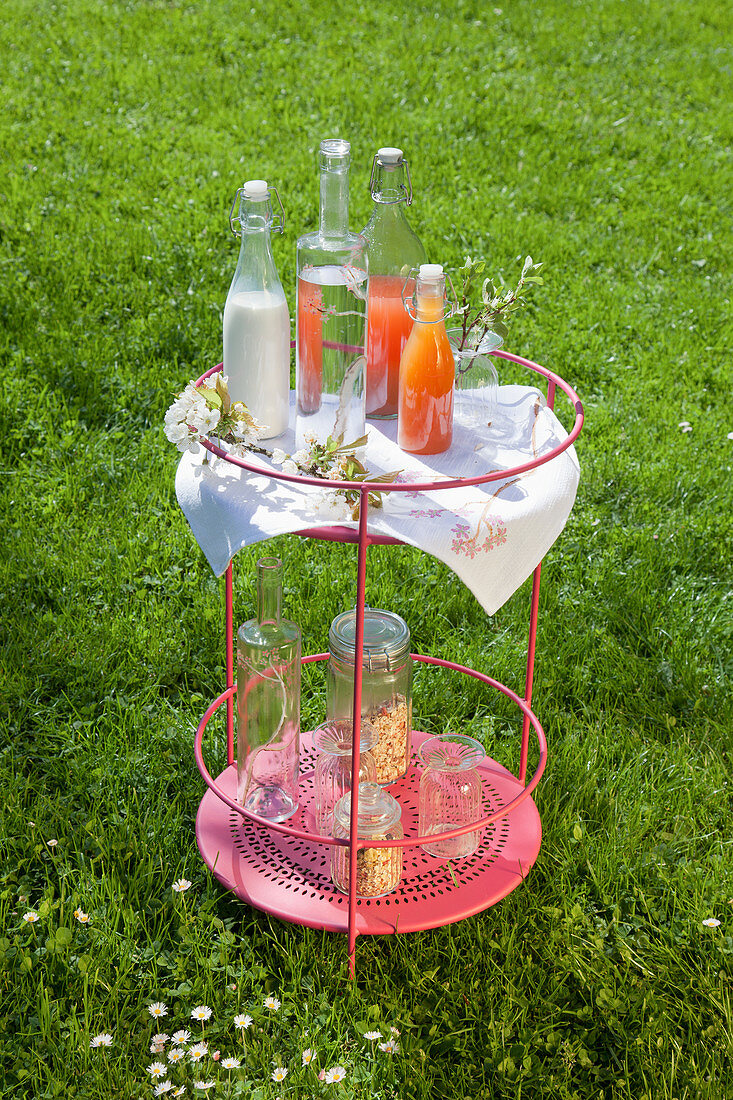 Erfrischungsgetränke in Flaschen und zarte Kirschblüten auf rundem Beistelltisch im Garten