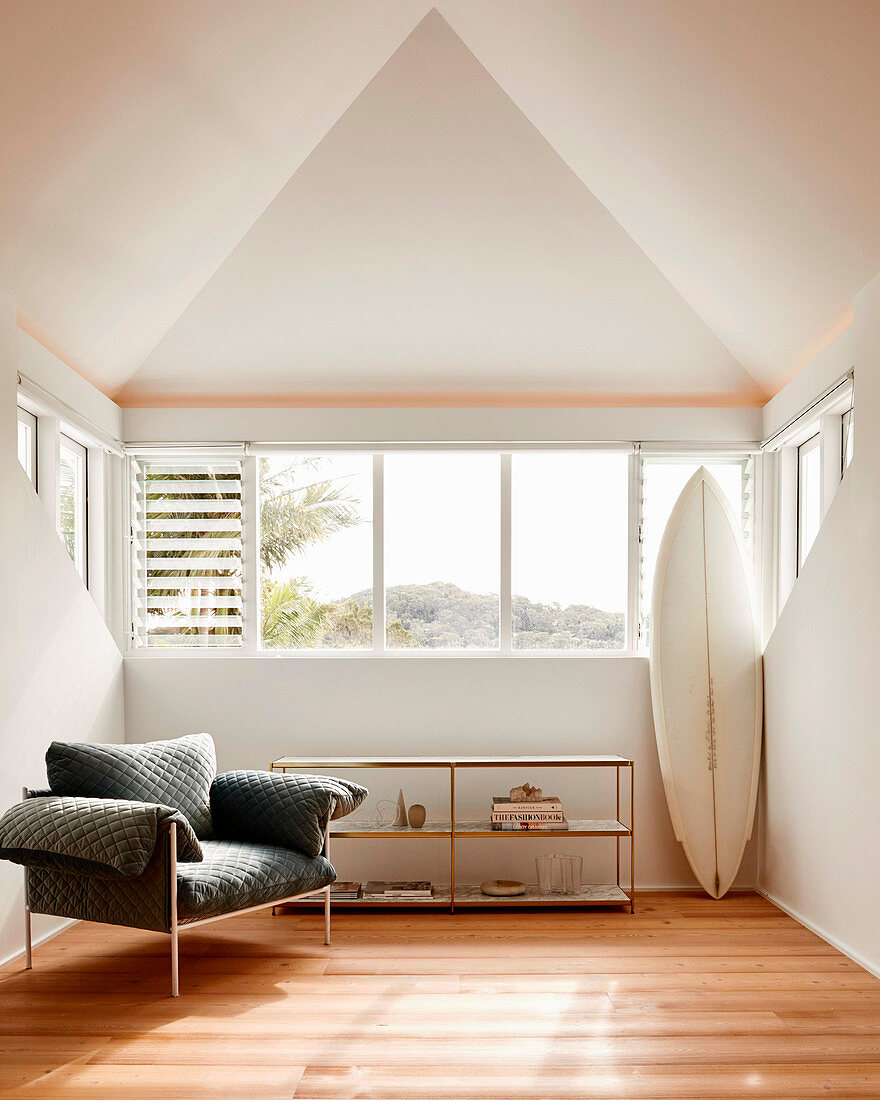 Designer armchair, shelf and surfboard in a bright room with a pointed roof