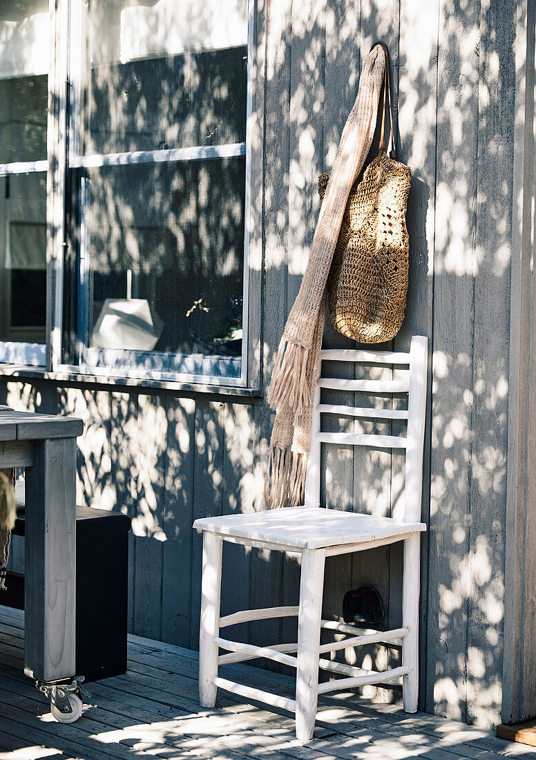 Chair on wooden terrace, scarf and bag above