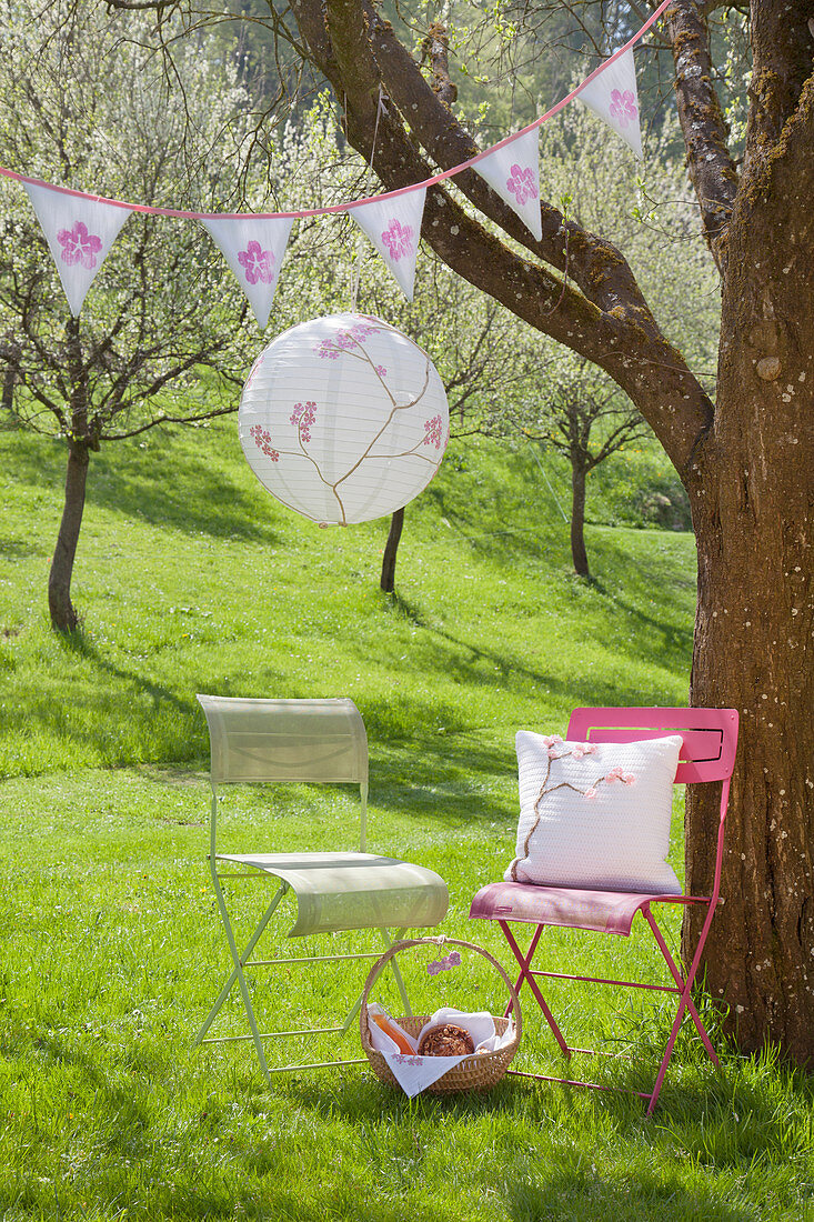 Romantischer Platz unter blühendem Kirschbaum mit Lampion und Wimpelkette: DIY-Kissen auf Stuhl, daneben umwickelter Ast mit Häkelblüten