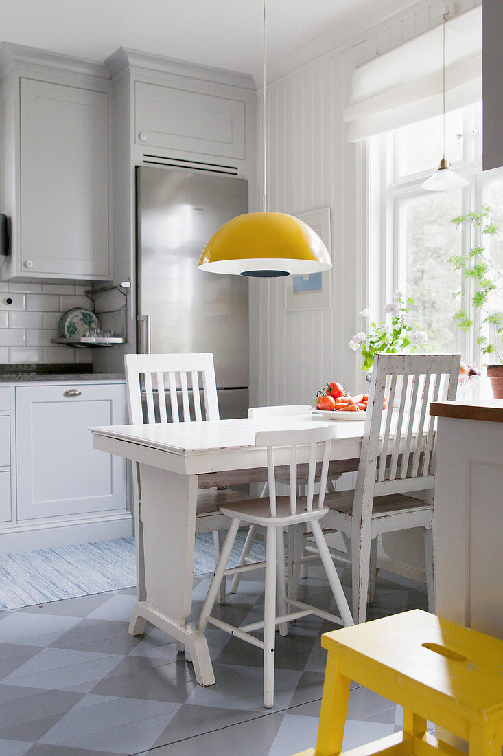 White wooden table and chairs below pendant lamp in kitchen-dining room