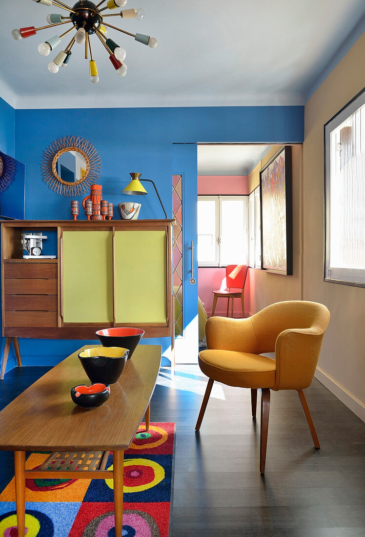Keramikschalen auf Couchtisch, Polstersessel und Highboard im Wohnzimmer mit blauer Wand