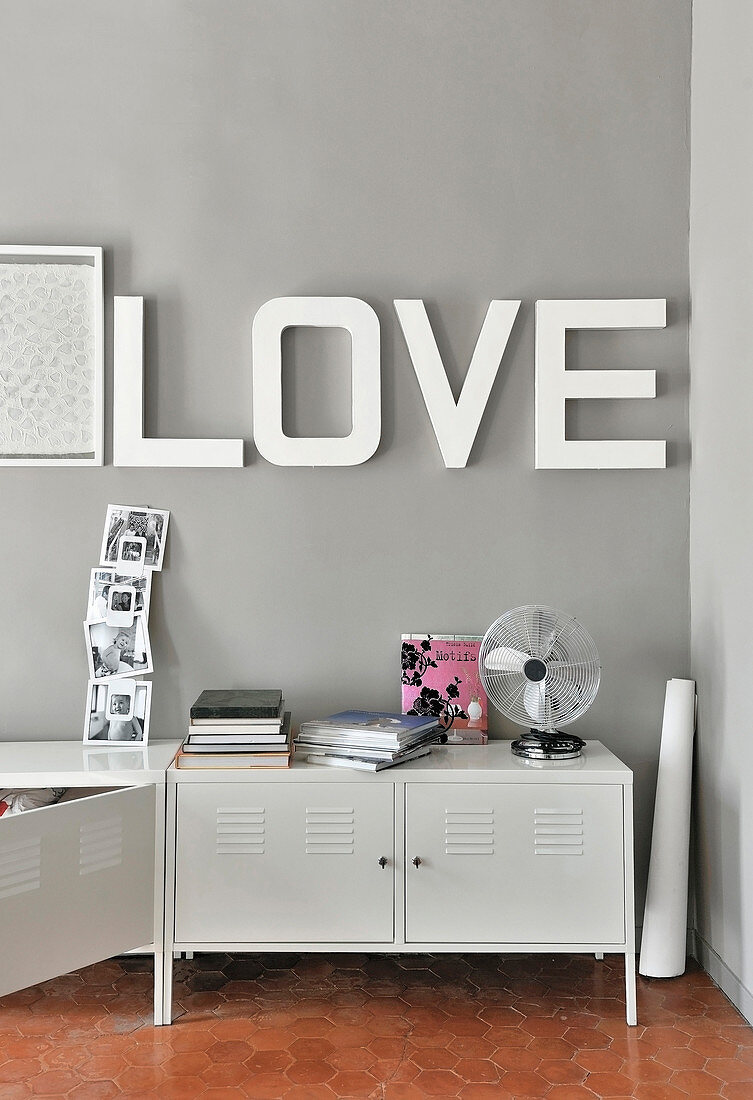 Schriftzug Love an grauer Wand über weißen Metallschränken