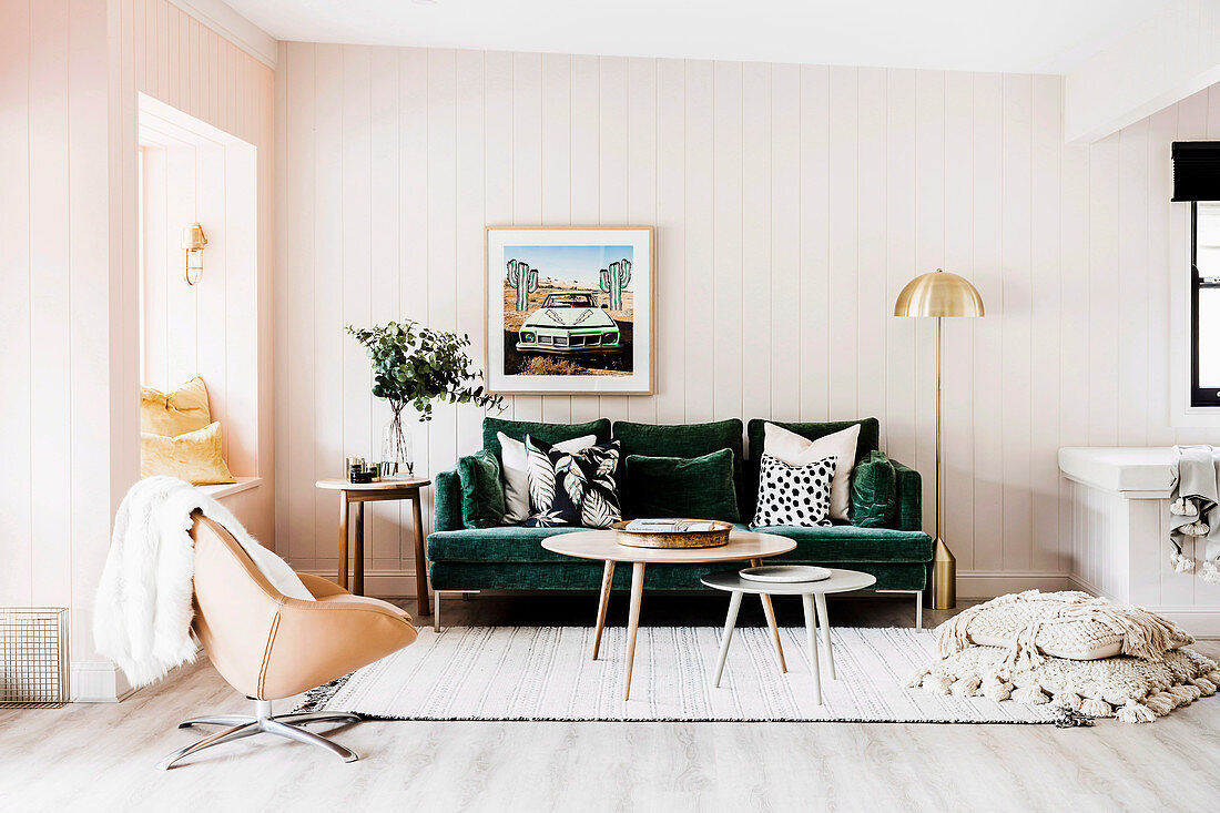 Grünes Sofa mit Dekokissen, Coffeetable und Drehsessel in Wohnzimmer mit weißer Holzverkleidung