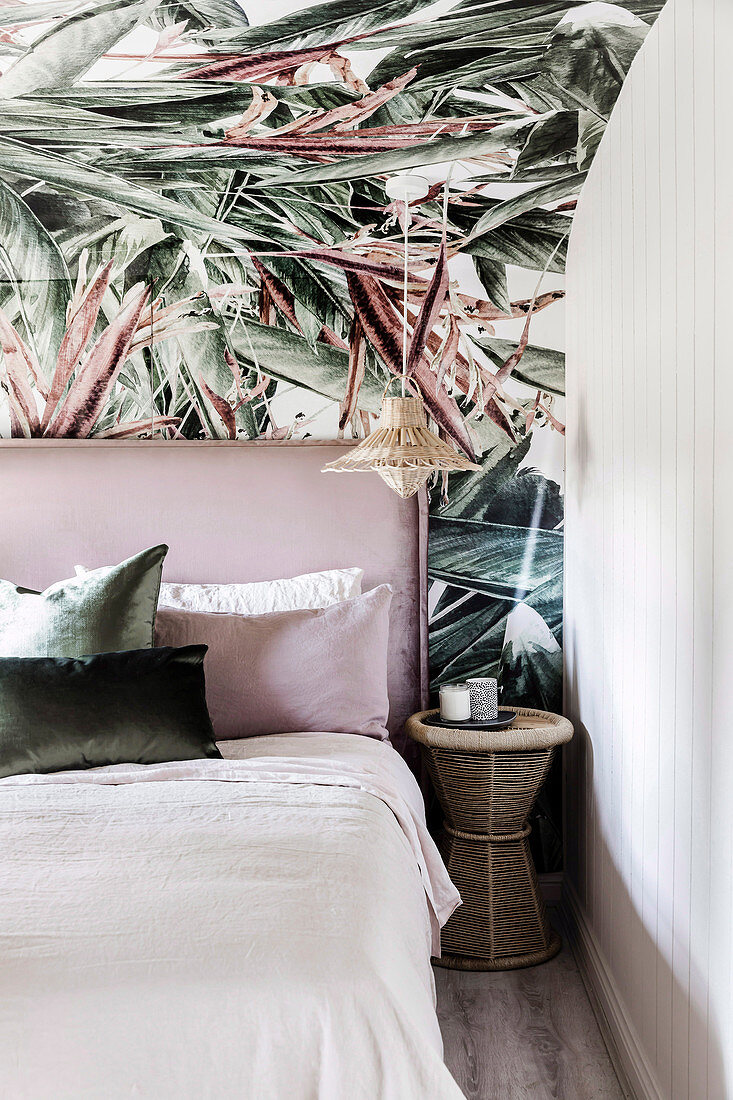 Bed with headboard on wallpapered wall with plant motif in bedroom