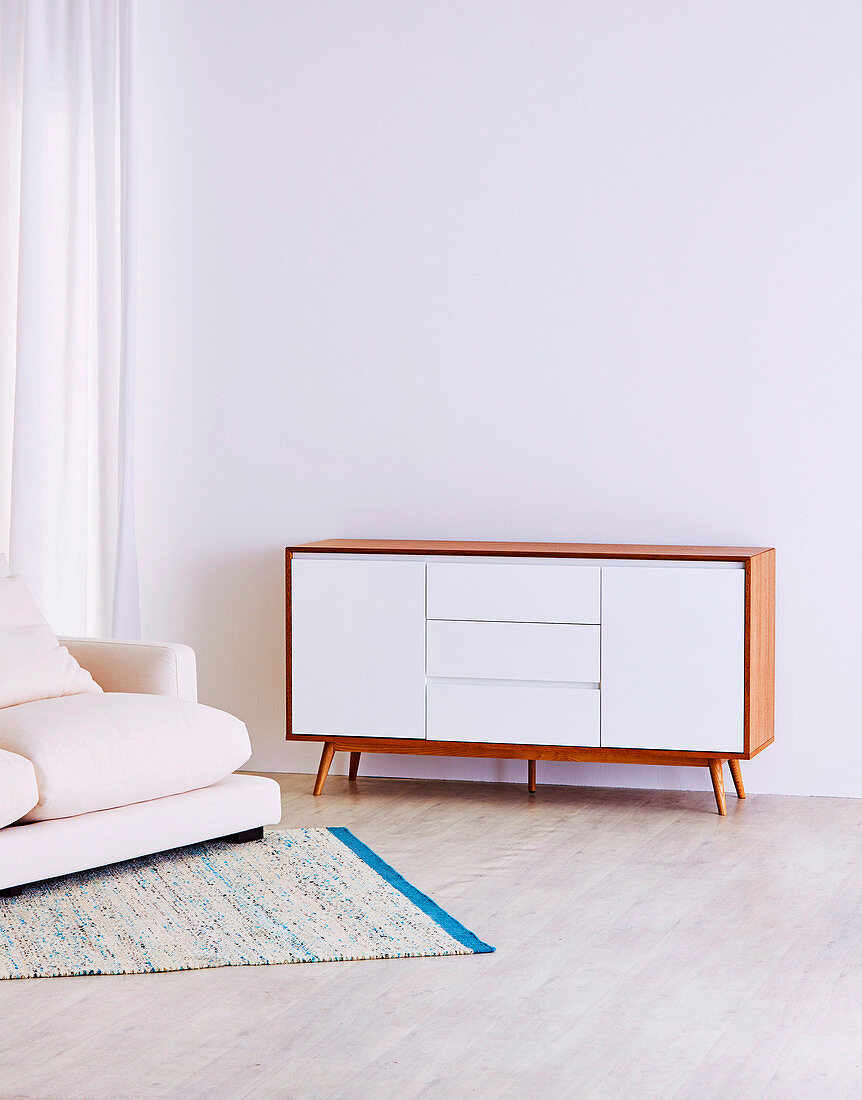 Retro sideboard and upholstered sofa against white wall