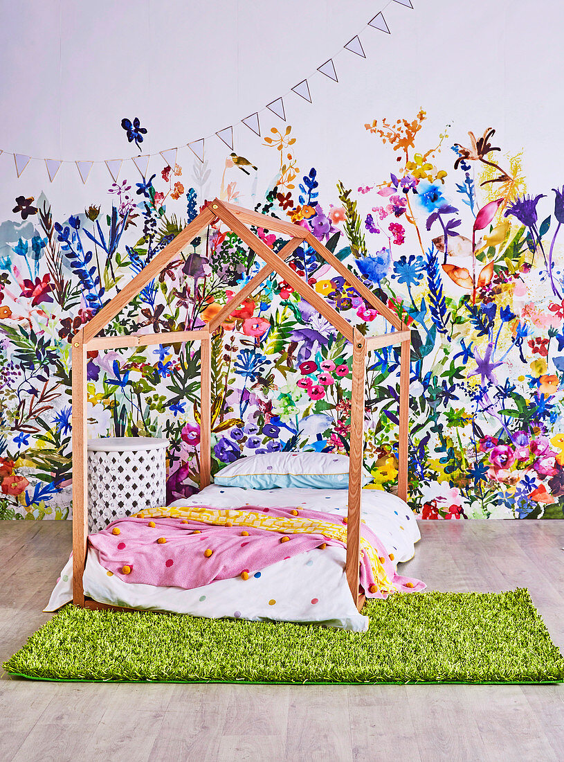 Bed frame in house shape in front of non-woven wallpaper with flower meadow in the children's room
