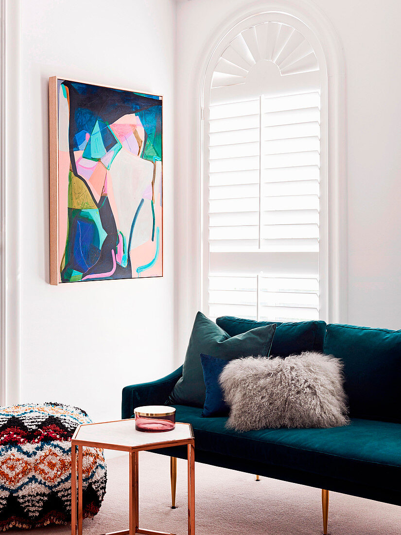Sofa with cushions, side table and pouf in front of arched window and artwork