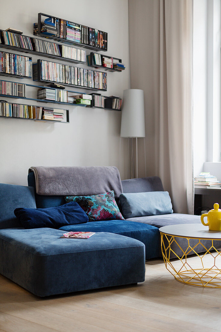 Grey-blue sofa below wall-mounted shelves in corner of living room