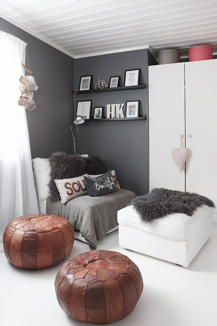 Zwei Lederpoufs und Sessel vor grauer Wand und einem Schrank