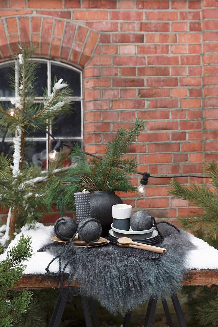 Tisch mit schwarzer Weihnachtsdeko und Tannenzweigen vor Backsteinhaus