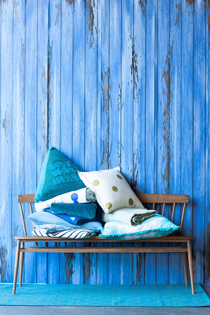 Wooden bench with cushions in front of a blue partition