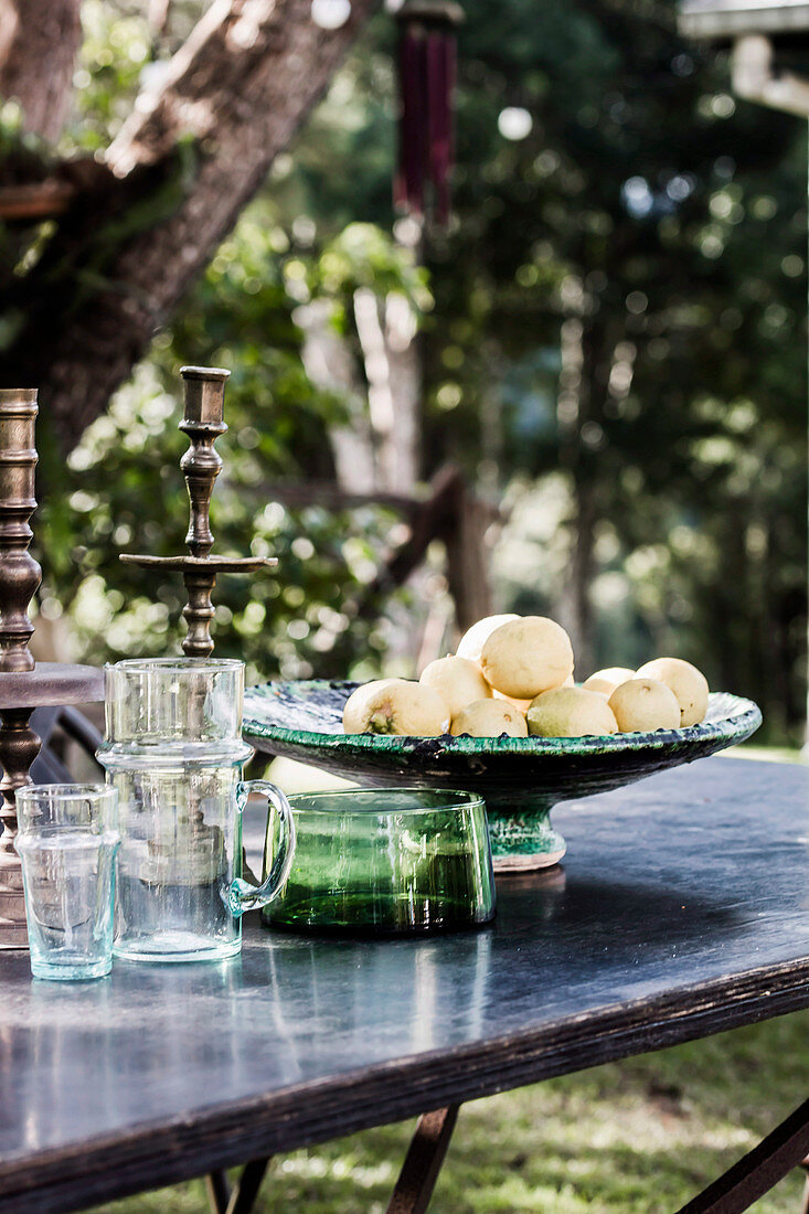 Gartentisch mit Gläsern und Obstschale unter Baum