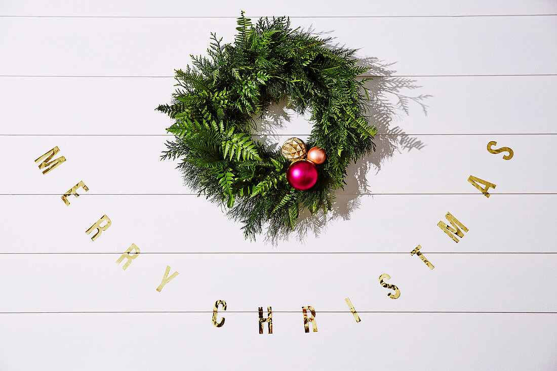 Weihnachtskranz und 'Merry Christmas' Aufschrift an weißer Holzwand