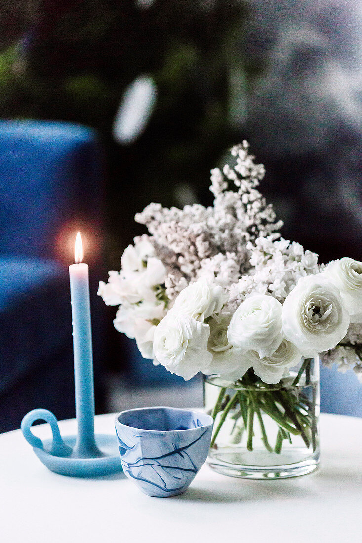Blue candle, small bowl and white bouquet on coffee table