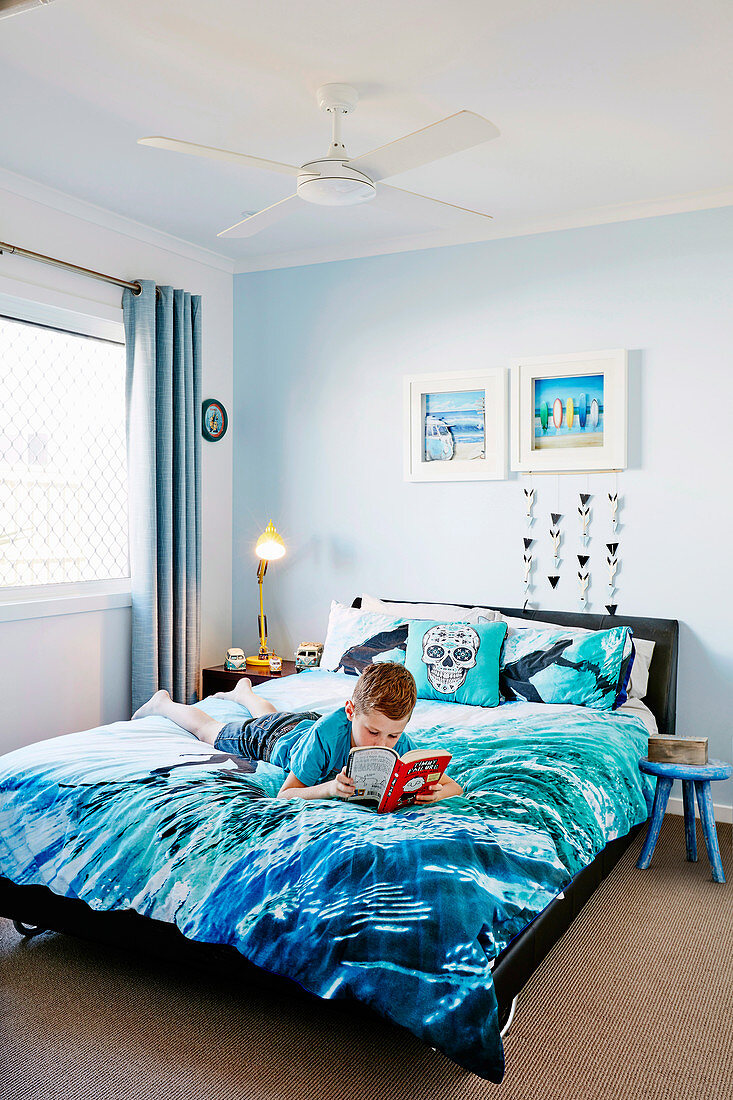 Junge mit Buch liegt auf Bett blauer Bettwäsche