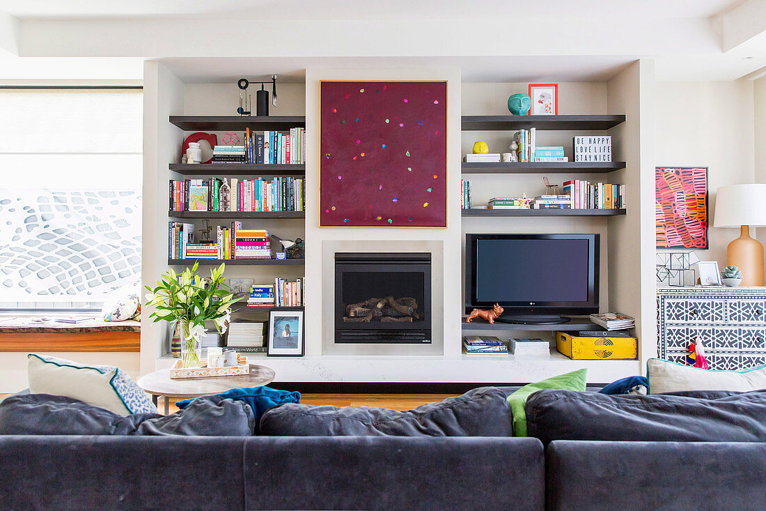 Blick über Polstersofa auf Wohnzimmerwand mit Kamin und Fernseher