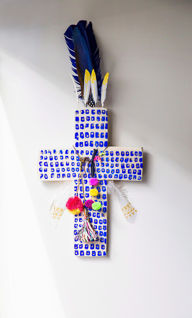 Blau gemustertes Kreuz mit Pompom und Federn dekoriert
