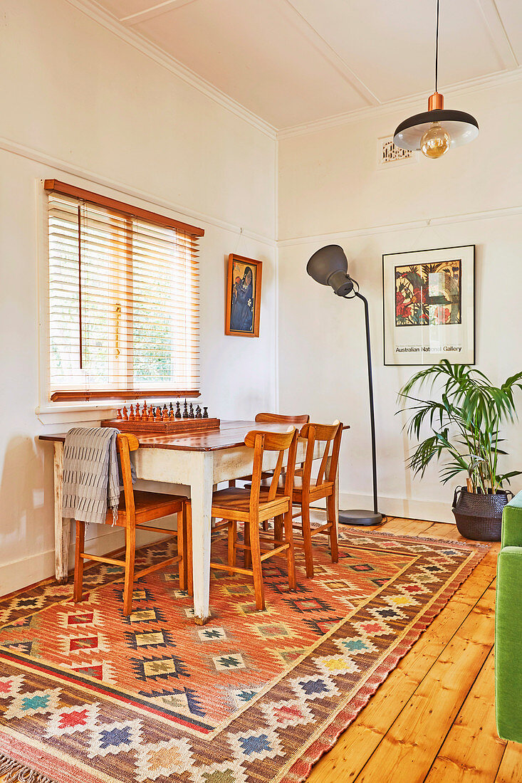 Holztisch mit Schachbrett und Stühlen vor Fenster, Stehlleuchte und Zimmerpflanze im Hintergrund