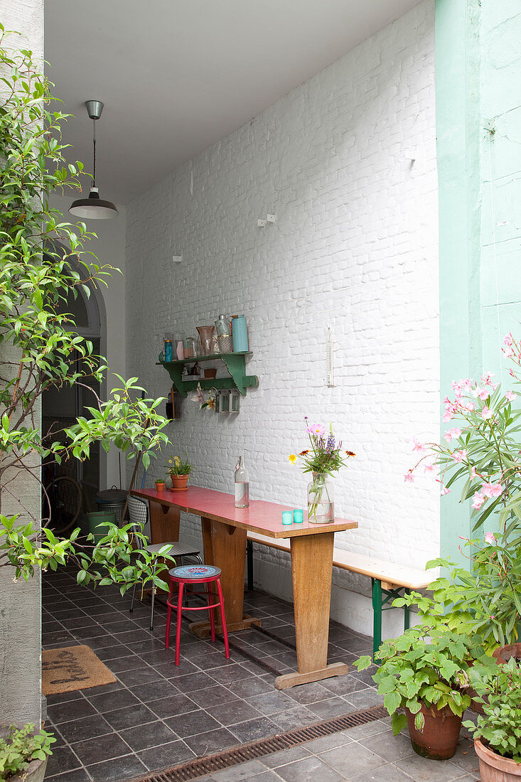 Wooden table, bench and stool on veranda with white brick wall
