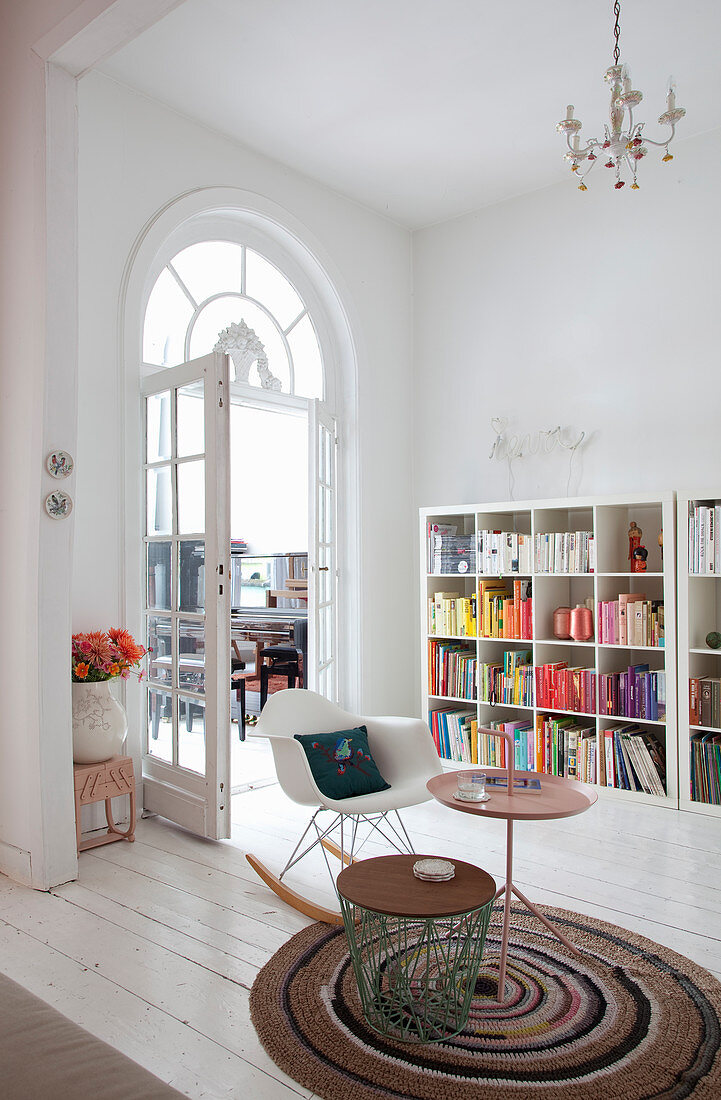 Beistelltische und Klassiker-Schaukelstuhl auf gehäkeltem Teppich vor Bücherregal