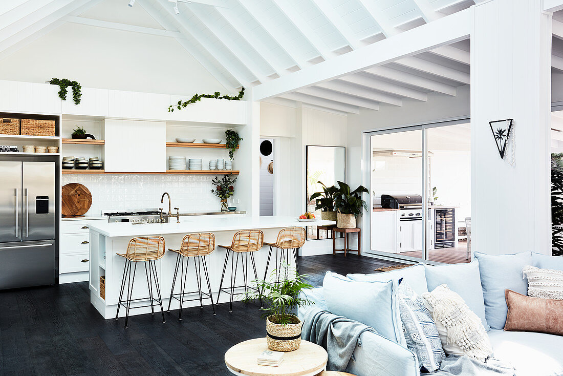 Sofa mit Kissen und weiße Küche mit Kücheninsel in offenem Wohnraum